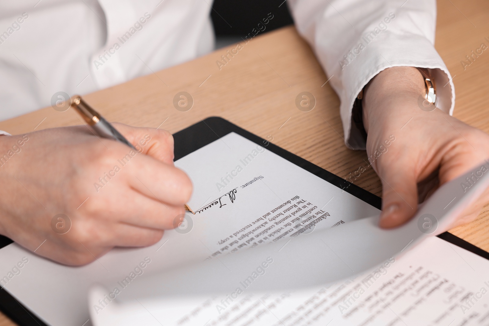 Photo of Woman putting signature on document at wooden table, closeup