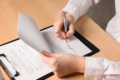 Photo of Woman putting signature on document at wooden table, closeup