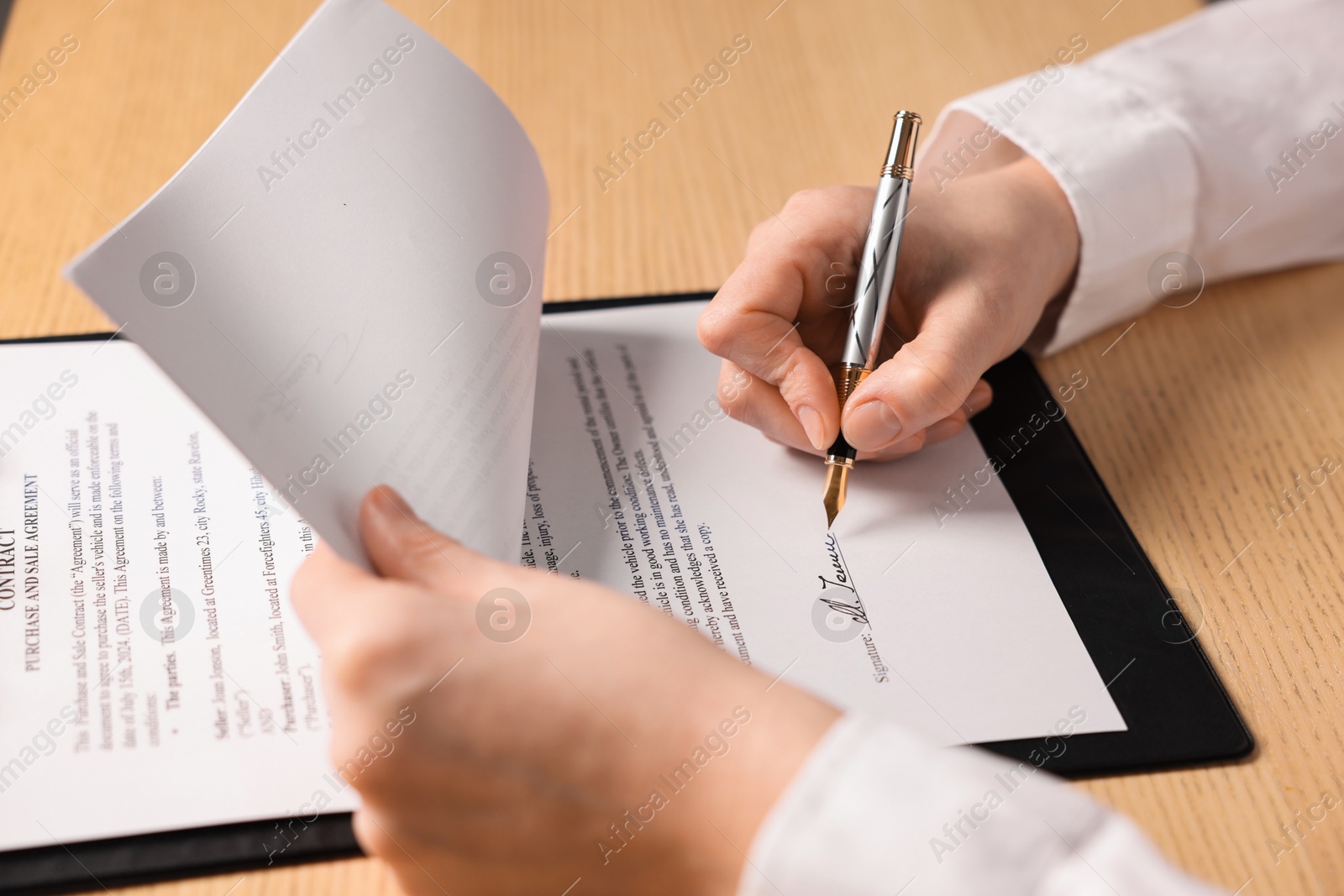 Photo of Woman putting signature on document at wooden table, closeup