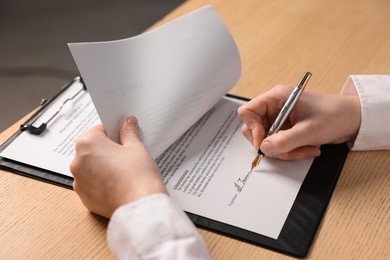 Photo of Woman putting signature on document at wooden table, closeup