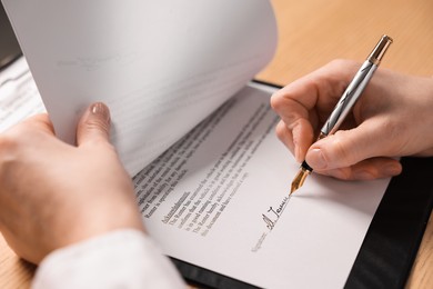 Photo of Woman putting signature on document at table, closeup