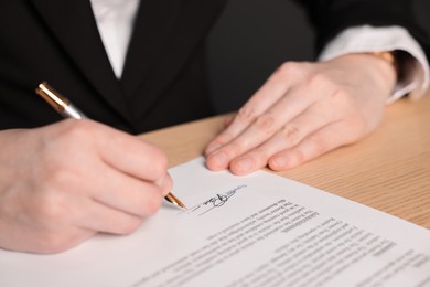 Photo of Woman putting signature on document at wooden table, closeup