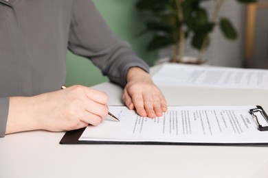 Photo of Woman putting signature on document at white table, closeup