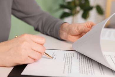 Photo of Woman putting signature on document at table, closeup