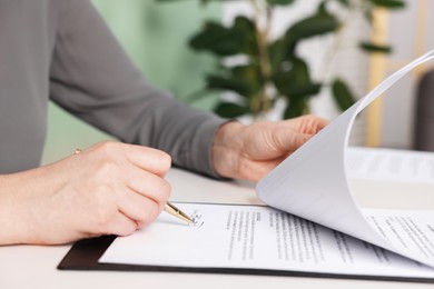 Photo of Woman putting signature on document at white table, closeup