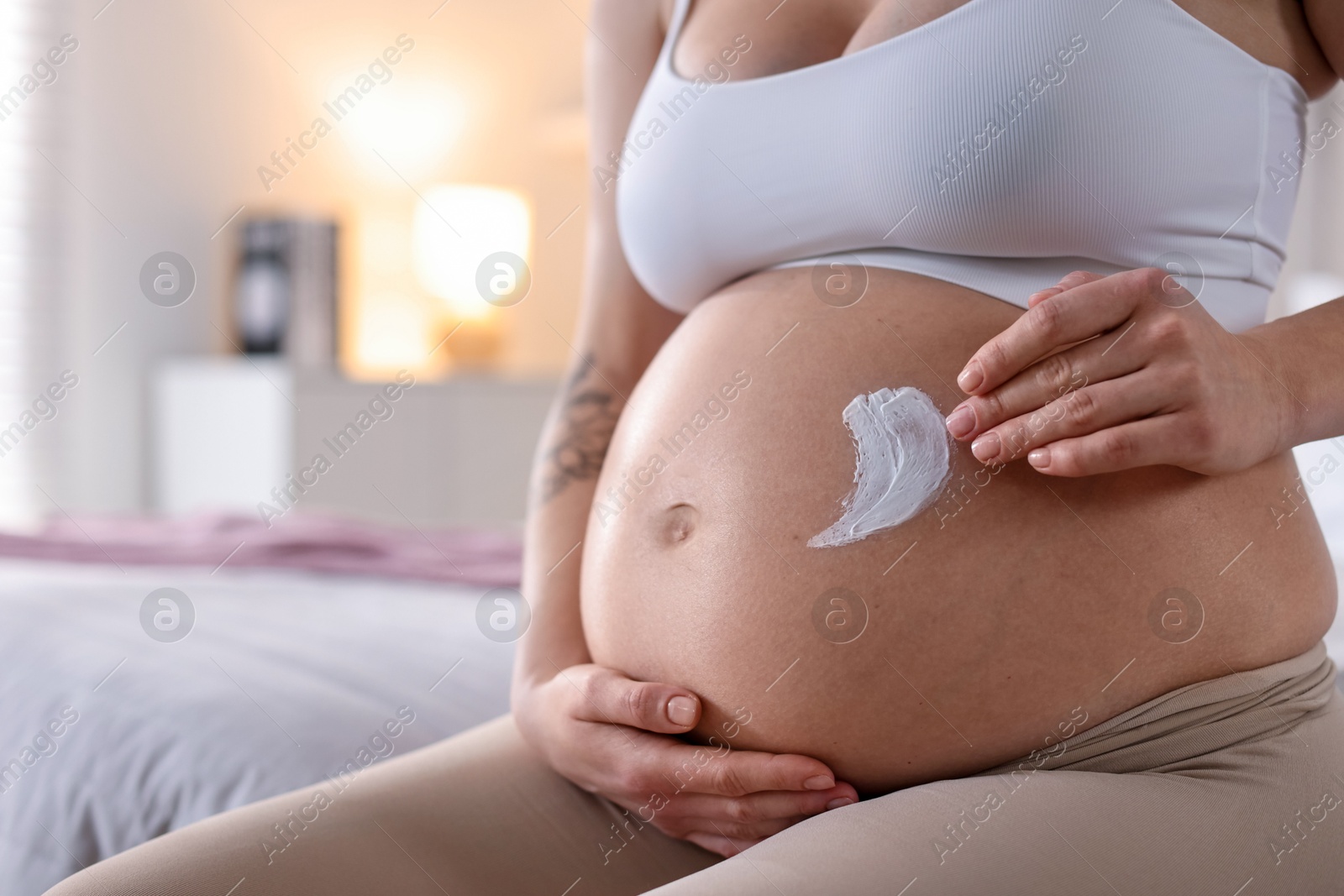 Photo of Pregnant woman applying cream on belly at home, closeup. Space for text