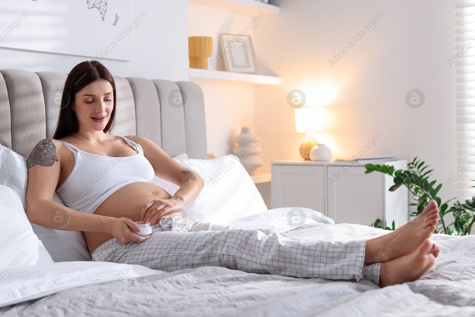 Photo of Pregnant woman with jar of cream on bed at home