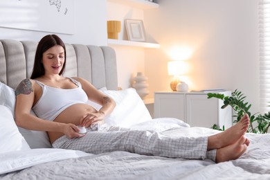 Photo of Pregnant woman with jar of cream on bed at home