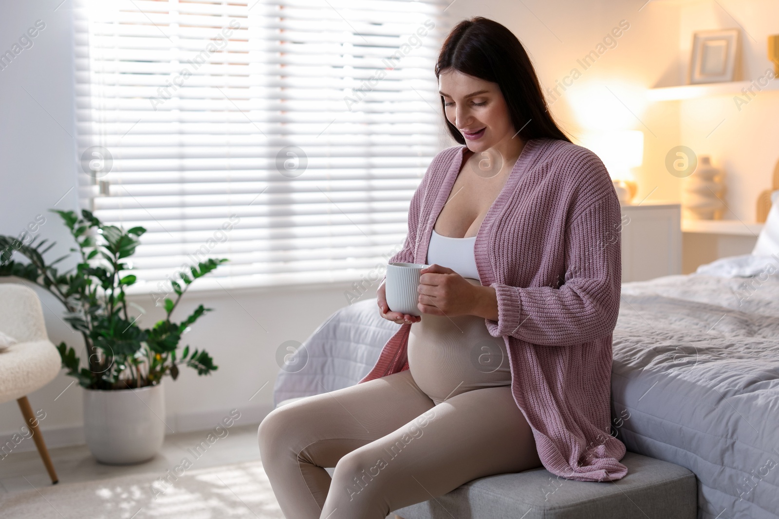 Photo of Beautiful pregnant with cup of drink at home, space for text