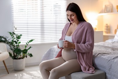 Photo of Beautiful pregnant with cup of drink at home, space for text