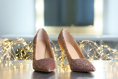 Photo of Shiny high heeled shoes and festive lights on grey table indoors, closeup