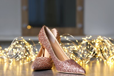 Shiny high heeled shoes and festive lights on grey table indoors, closeup