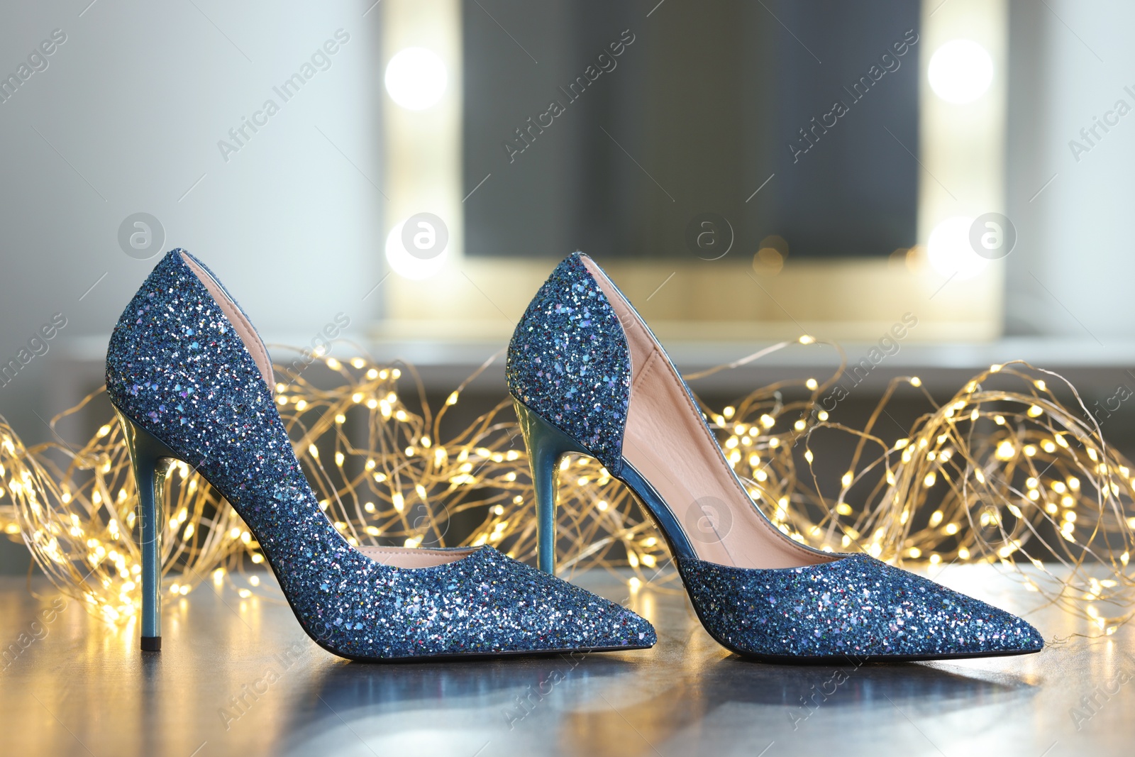 Photo of Shiny high heeled shoes and festive lights on grey table indoors, closeup