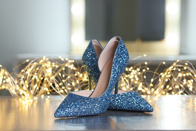 Shiny high heeled shoes and festive lights on grey table indoors, closeup