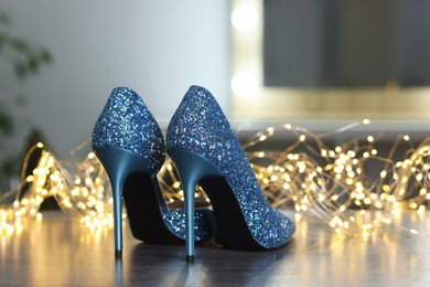 Shiny high heeled shoes and festive lights on grey table indoors, closeup