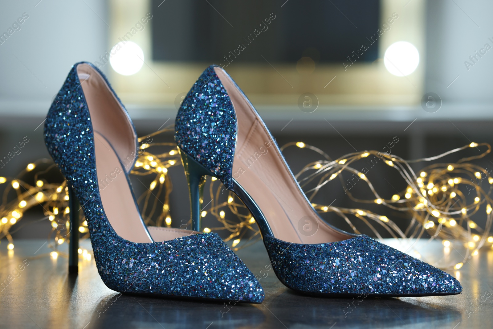 Photo of Shiny high heeled shoes and festive lights on grey table indoors, closeup