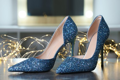 Shiny high heeled shoes and festive lights on grey table indoors, closeup