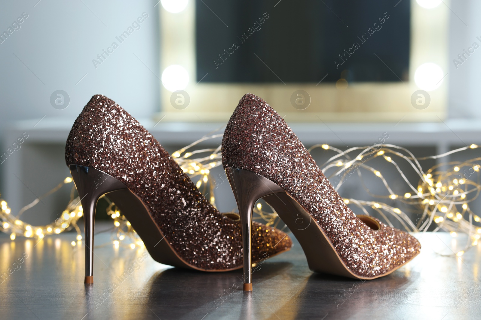 Photo of Shiny high heeled shoes and festive lights on grey table indoors, closeup