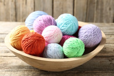 Photo of Balls of colorful yarn in bowl on wooden table, closeup