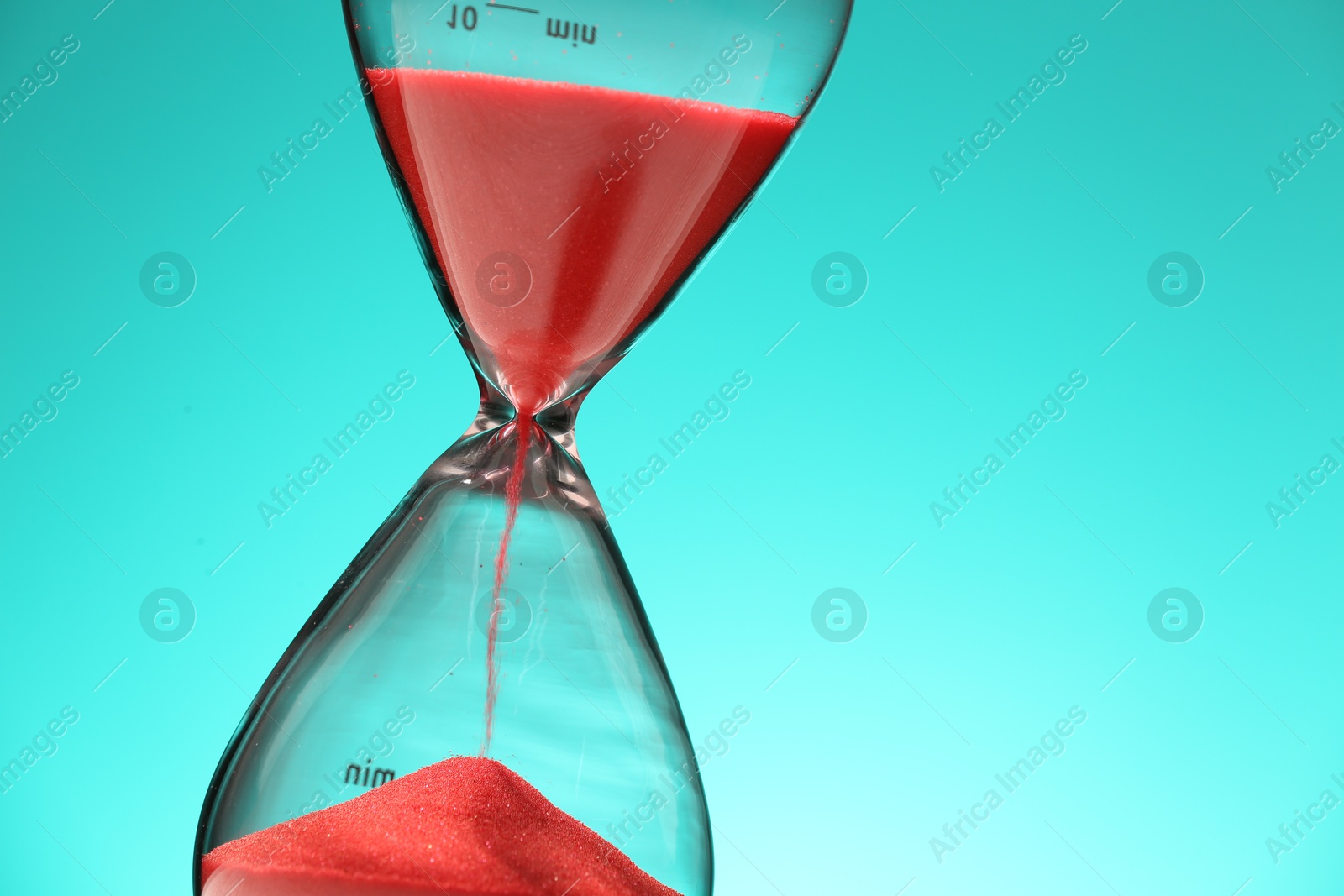 Photo of Hourglass with red flowing sand on turquoise background, closeup. Space for text