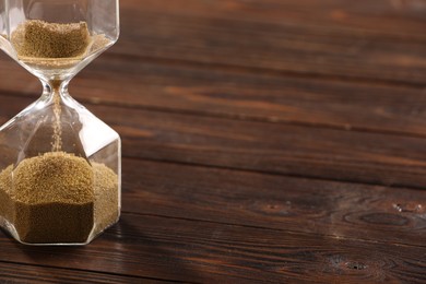 Photo of Hourglass with flowing sand on wooden table, closeup. Space for text