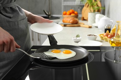 Photo of Woman taking fried eggs from frying pan in kitchen, closeup