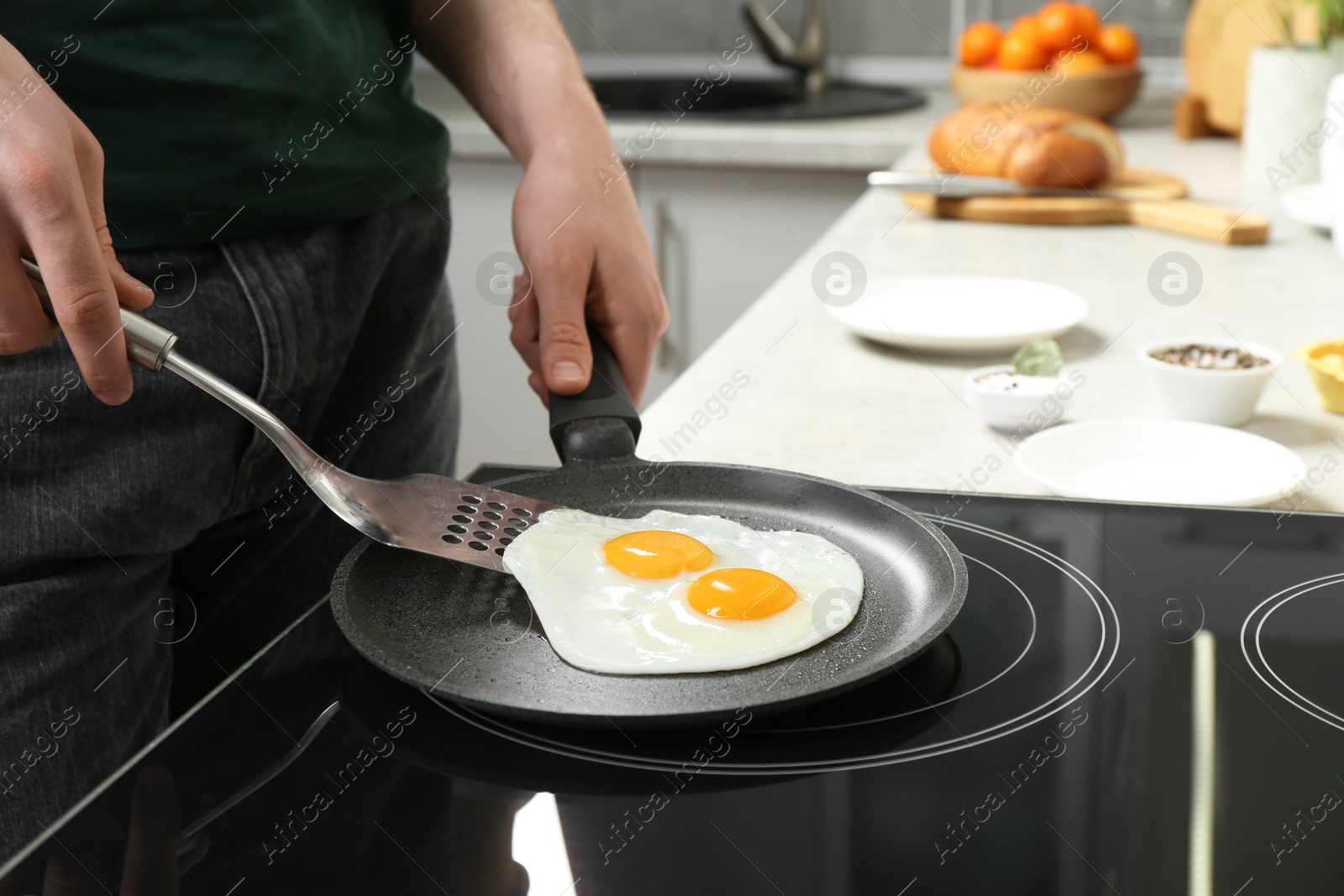 Photo of Man taking fried eggs from frying pan in kitchen, closeup