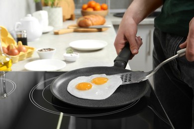 Photo of Man taking fried eggs from frying pan in kitchen, closeup