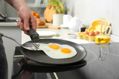 Photo of Man taking fried eggs from frying pan in kitchen, closeup