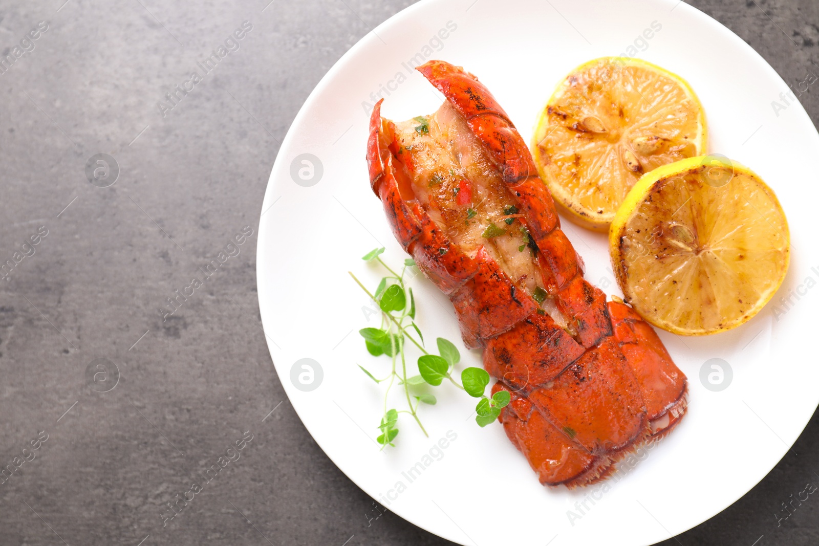 Photo of Delicious lobster tail with microgreens and slices of lemon on grey textured table, top view. Space for text