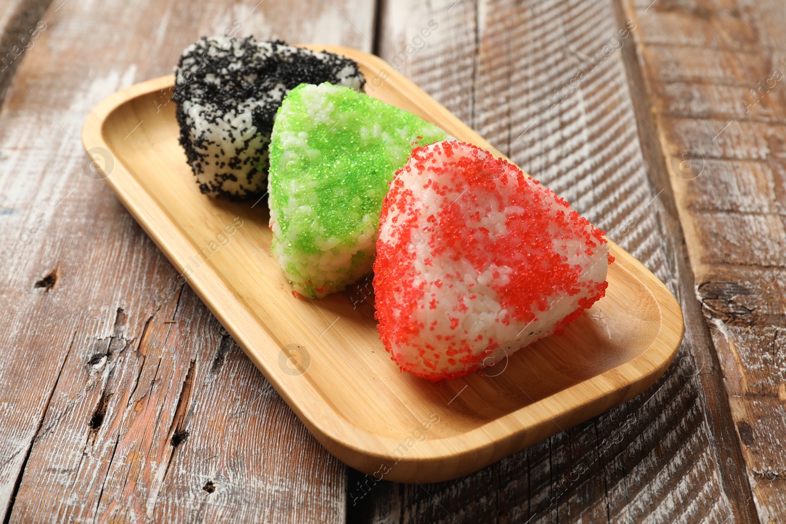 Photo of Tasty tobiko onigiri (Japanese rice balls) served on wooden table, closeup