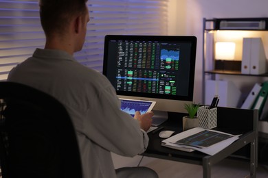 Photo of Stock exchange. Man working in office at night, back view