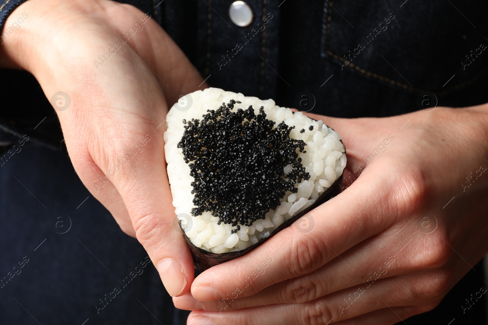 Photo of Woman with tasty tobiko onigiri (Japanese rice ball), closeup