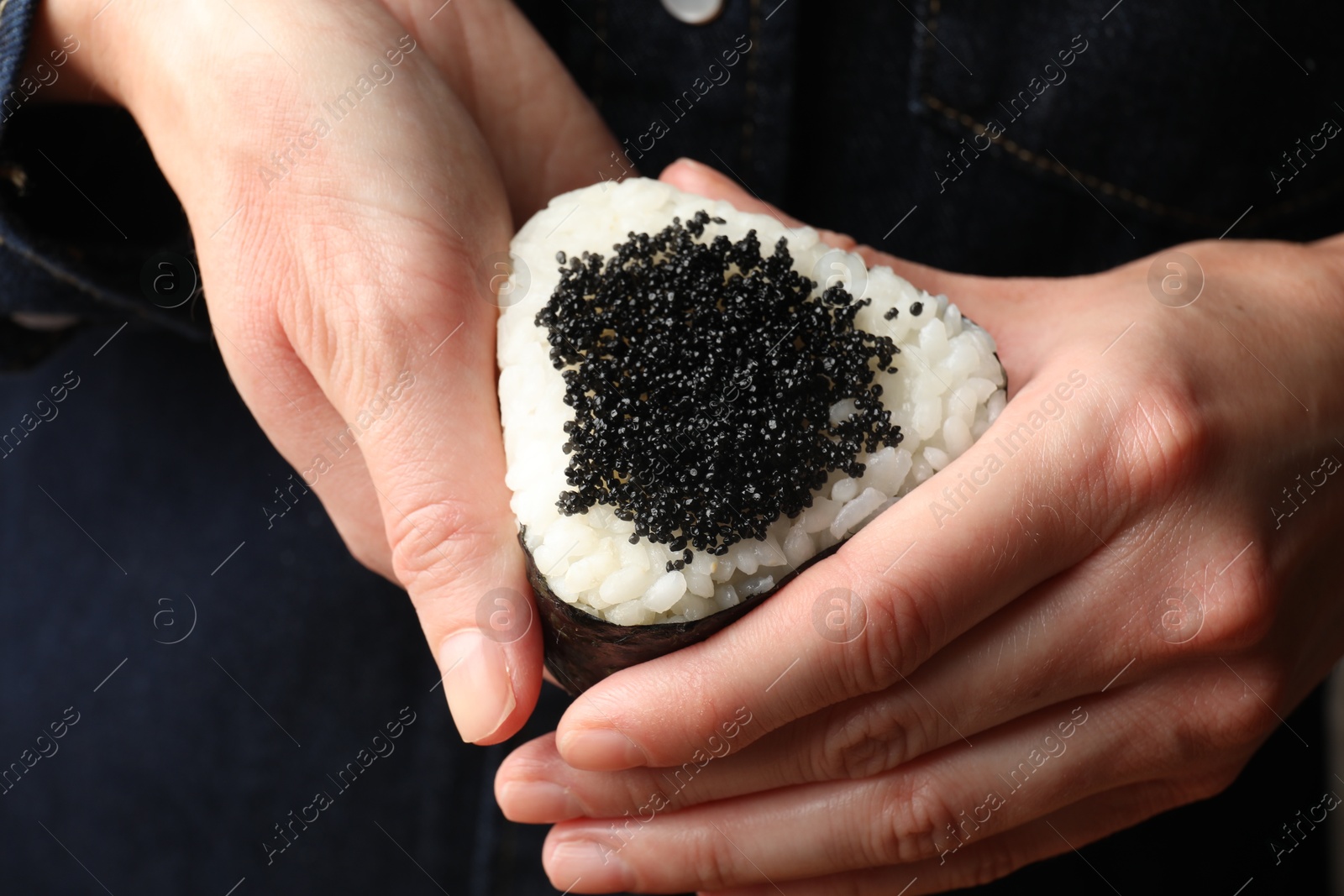 Photo of Woman with tasty tobiko onigiri (Japanese rice ball), closeup