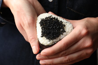 Photo of Woman with tasty tobiko onigiri (Japanese rice ball), closeup