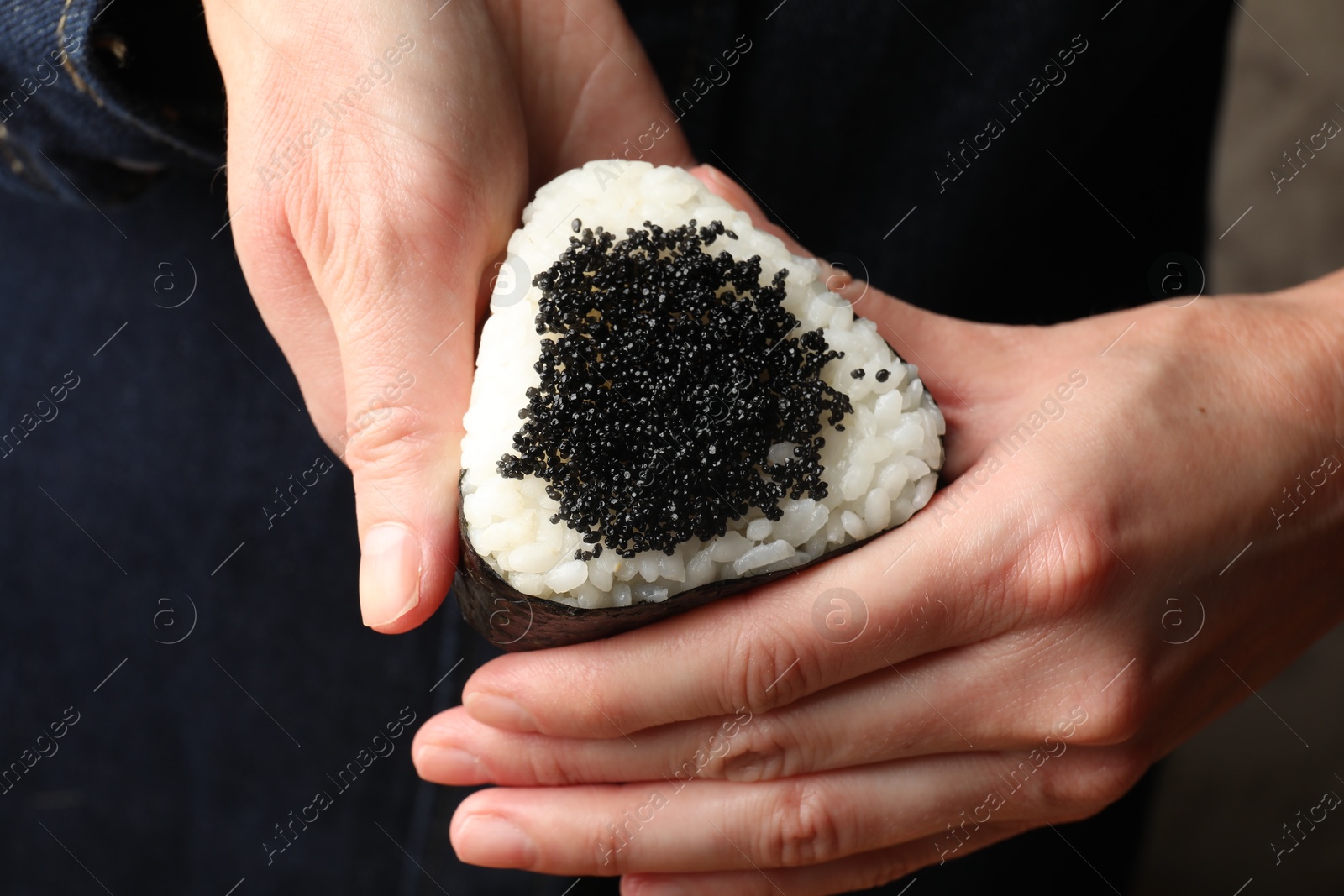 Photo of Woman with tasty tobiko onigiri (Japanese rice ball), closeup