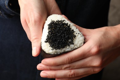 Photo of Woman with tasty tobiko onigiri (Japanese rice ball), closeup