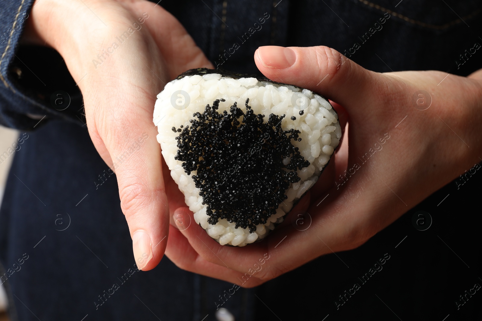 Photo of Woman with tasty tobiko onigiri (Japanese rice ball), closeup