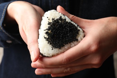 Photo of Woman with tasty tobiko onigiri (Japanese rice ball), closeup