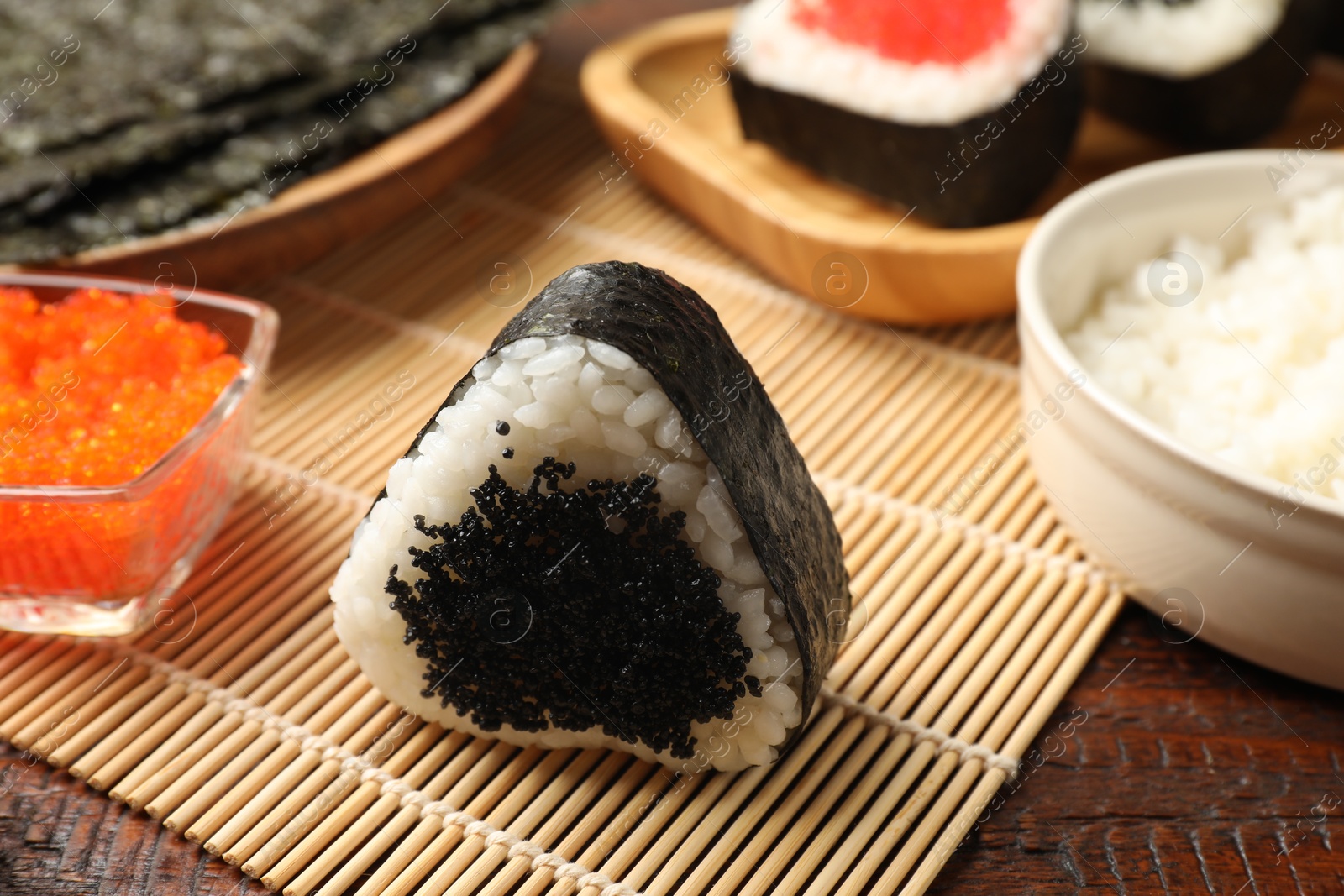 Photo of Tasty tobiko onigiri (Japanese rice ball) and ingredients on wooden table, closeup