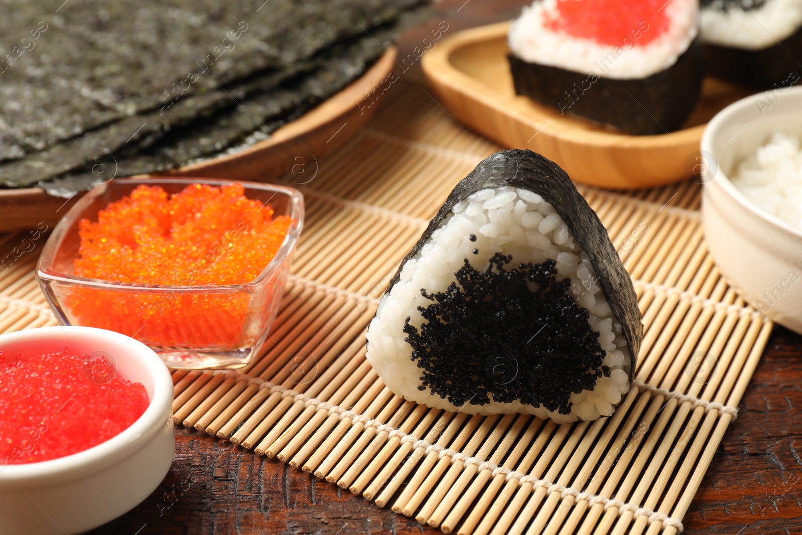 Photo of Tasty tobiko onigiri (Japanese rice ball) and ingredients on wooden table, closeup