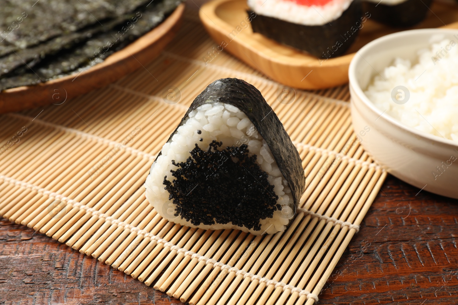 Photo of Tasty tobiko onigiri (Japanese rice ball) and ingredients on wooden table, closeup