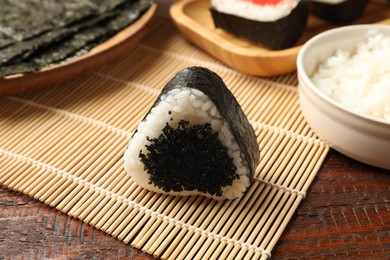 Photo of Tasty tobiko onigiri (Japanese rice ball) and ingredients on wooden table, closeup