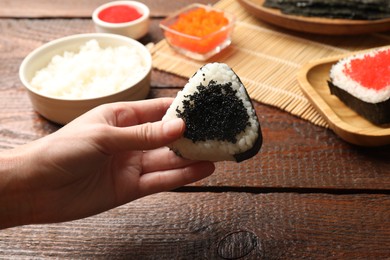 Photo of Woman with tasty tobiko onigiri (Japanese rice balls) at wooden table, closeup