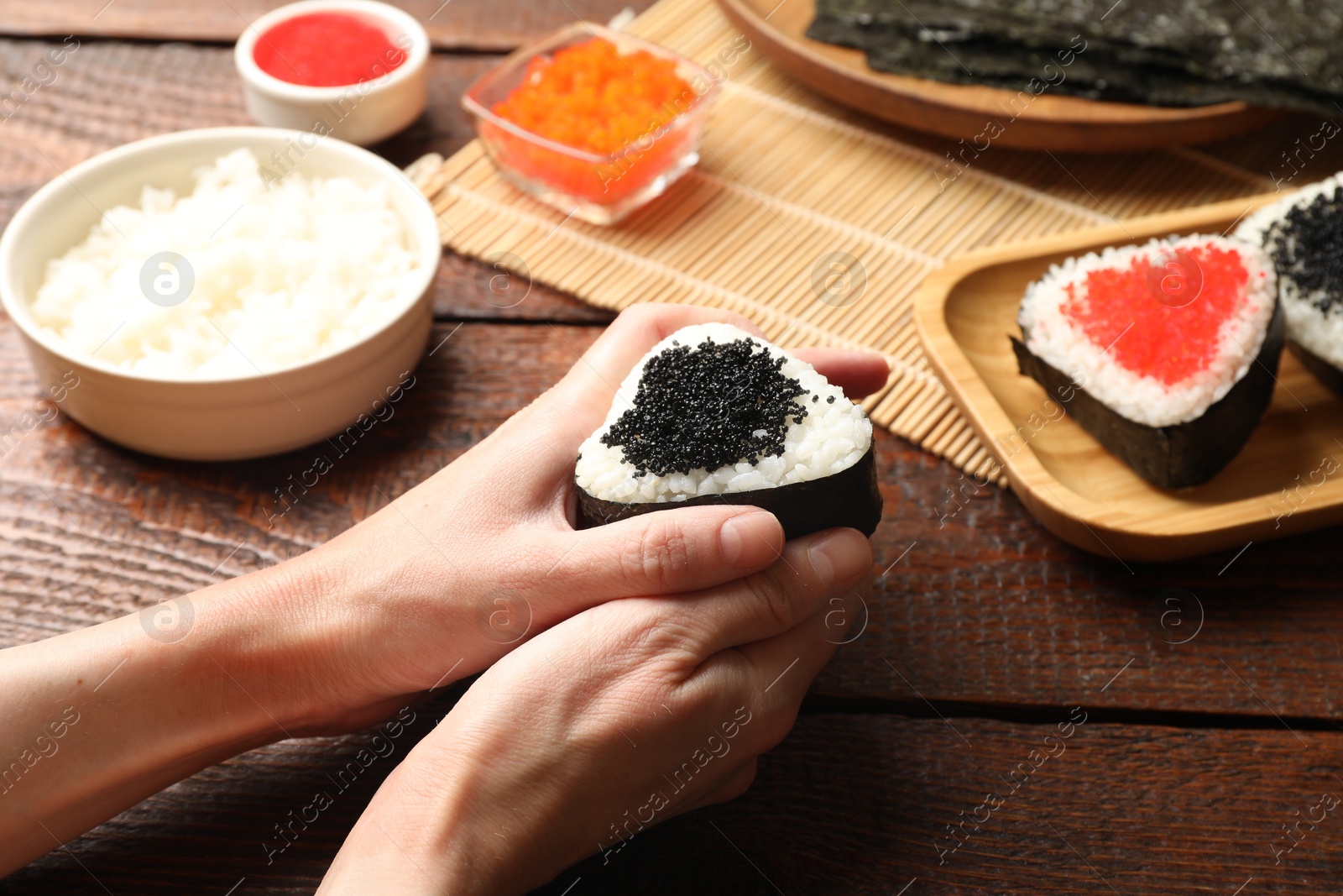 Photo of Woman with tasty tobiko onigiri (Japanese rice balls) at wooden table, closeup