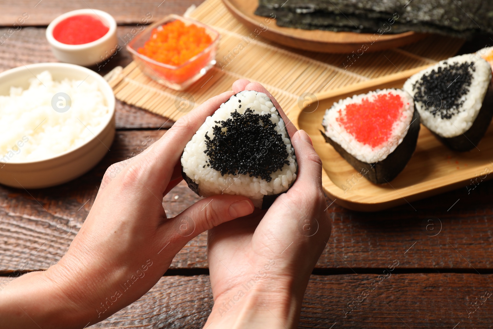 Photo of Woman with tasty tobiko onigiri (Japanese rice balls) at wooden table, closeup