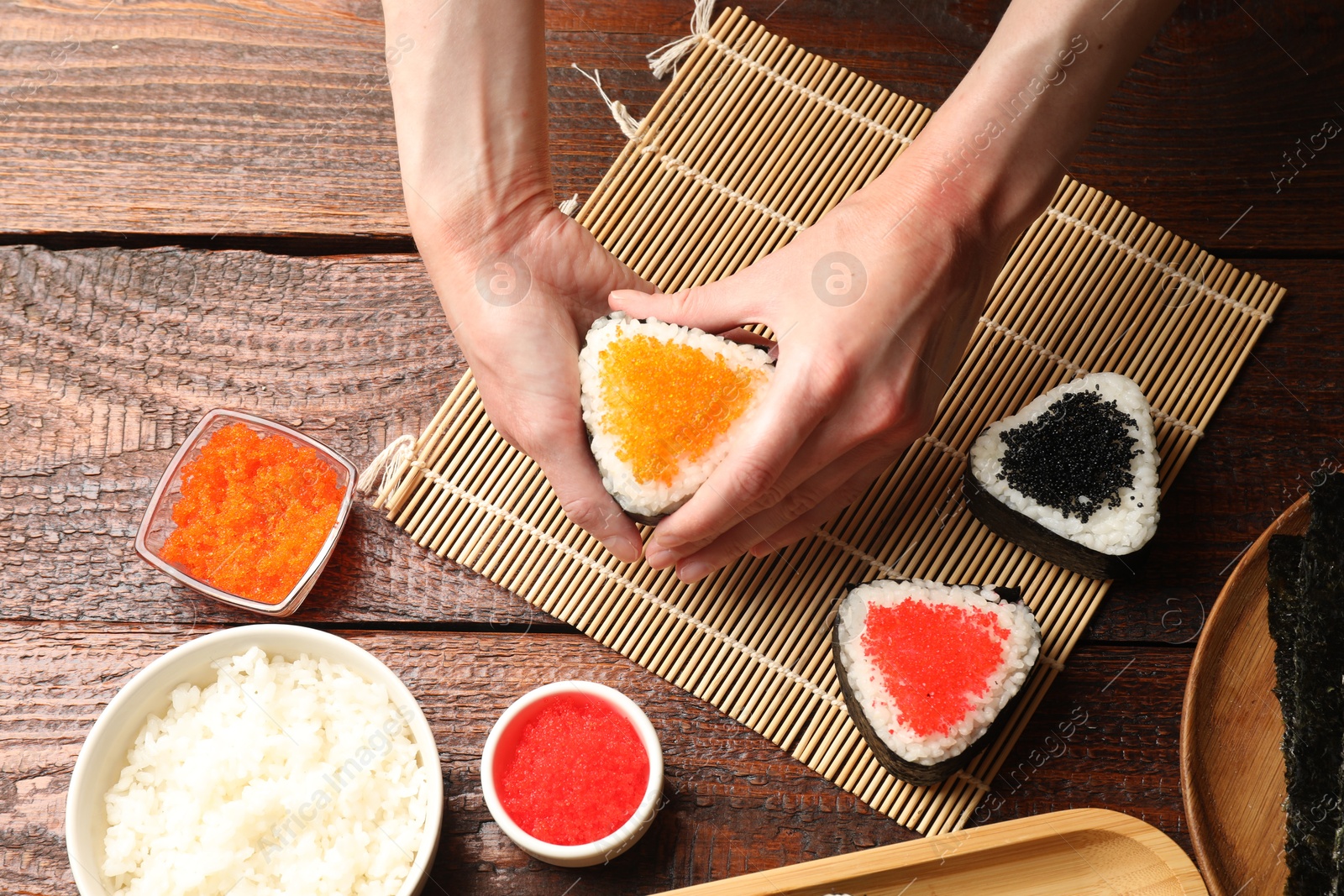 Photo of Woman with tasty tobiko onigiri (Japanese rice balls) at wooden table, top view