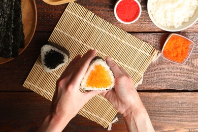 Photo of Woman with tasty tobiko onigiri (Japanese rice balls) at wooden table, top view