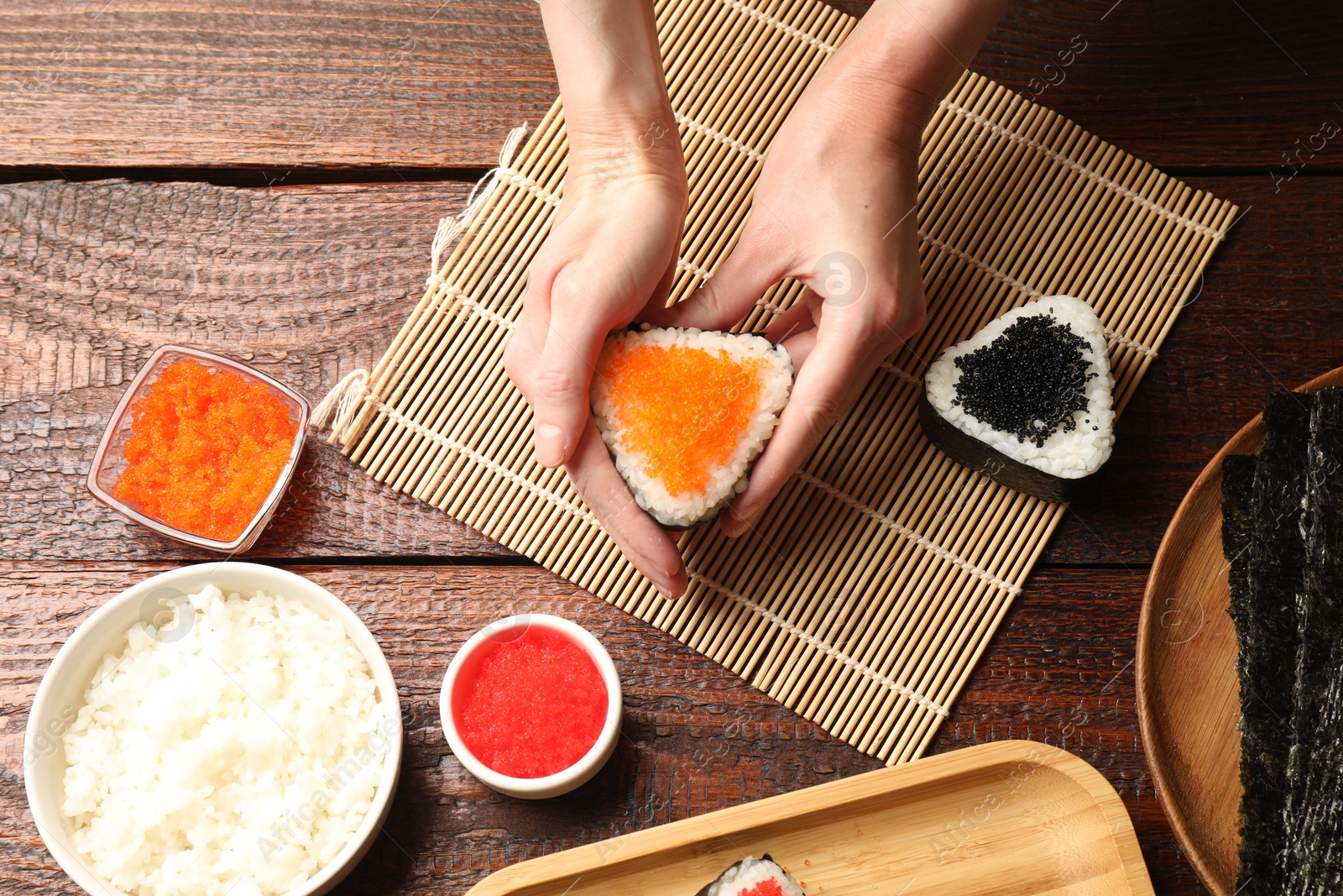 Photo of Woman with tasty tobiko onigiri (Japanese rice balls) at wooden table, top view