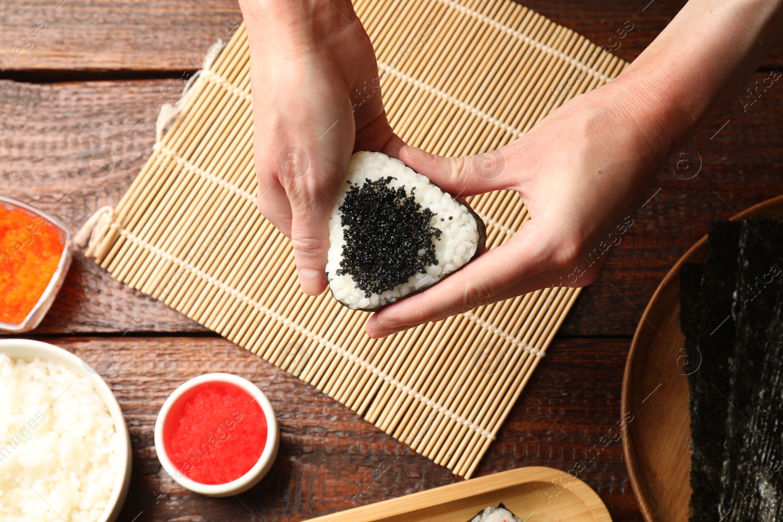 Photo of Woman with tasty tobiko onigiri (Japanese rice ball) at wooden table, top view